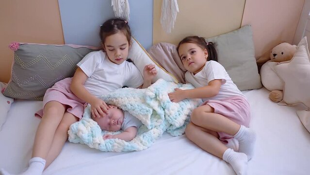 Three little siblings kids lying in bed at home, newborn baby with sisters.