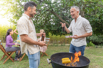 Multiethnic middle-aged friends around the barbecue smiling happy and laughing together. Joy concept.