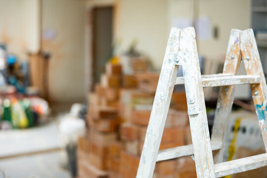 Ladder with stains of paint and plaster at indoor building construction site, various construction materials stacked on background