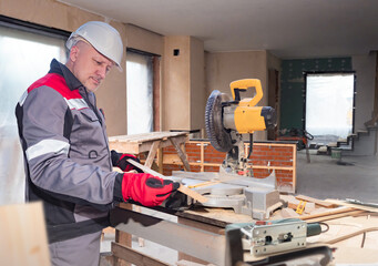 Man saws parquet board. Builder stands next to circular saw. Builder is preparing parquet board for repair. Stationary circular saw on table. Man builder in building under construction