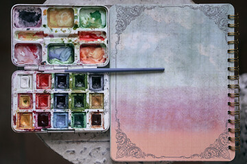 closeup of a ring binder box of watercolors with paint of many colors and small fine brush