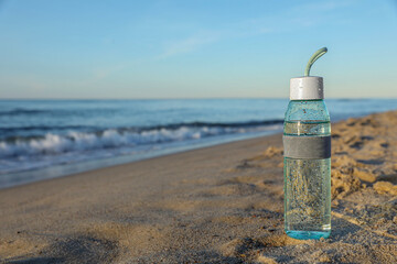 Fototapeta na wymiar Glass bottle with water on wet sand near sea. Space for text