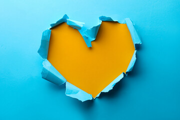 Torn heart shaped hole in light blue paper on yellow background
