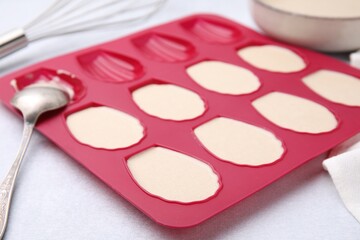 Baking mold for madeleine cookies with batter on white table, closeup