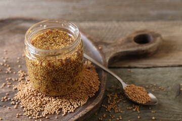 Jar and spoon of whole grain mustard on wooden table. Space for text