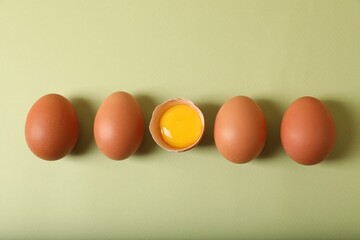 Cracked and whole chicken eggs on olive background, flat lay