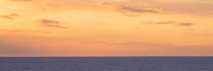 Beautiful sunset sky background with clouds. Colorful clouds over the ice-covered sea. Picturesque winter landscape. The nature of the Arctic. Polar region. Wide panoramic background for design.