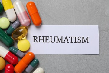 Sheet of paper with word Rheumatism and many different pills on light grey table, flat lay