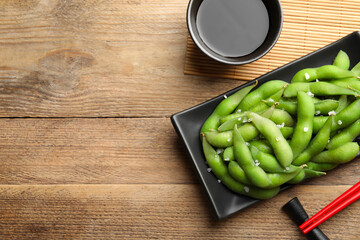 Green edamame beans in pods served with soy sauce on wooden table, flat lay. Space for text