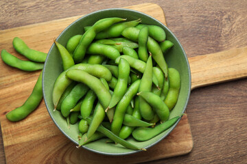 Bowl with green edamame beans in pods on wooden table, top view