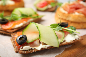 Tasty rye crispbreads with salmon, cream cheese and vegetables on wooden board. closeup