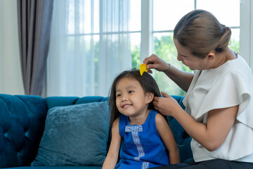 Asian young mother combing lovely daughter hair in living room