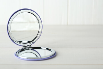 Stylish cosmetic pocket mirror on white wooden table. Space for text