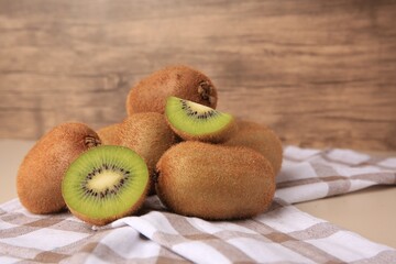 Heap of whole and cut fresh kiwis on beige table, space for text