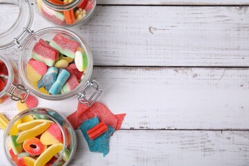 Tasty jelly candies in different jars on white wooden table, flat lay. Space for text