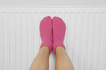 Woman warming legs on heating radiator near white wall, closeup
