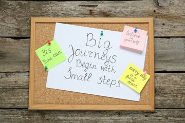 Corkboard with motivational quotes on wooden table, top view