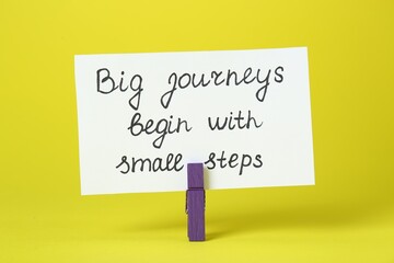 Card with phrase Big Journeys Begin With Small Steps and clothespin on yellow background....