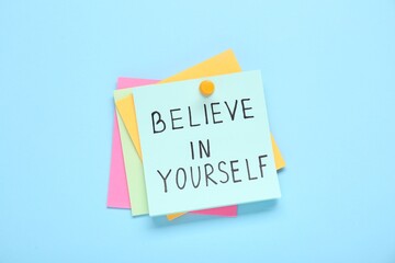 Notes with phrase Believe In Yourself on light blue background, top view. Motivational quote