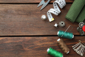 Threads and other sewing supplies on wooden table, flat lay. Space for text