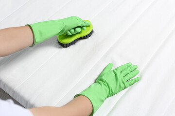 Woman in green gloves cleaning white mattress with brush, closeup