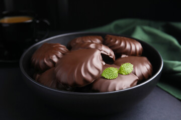 Delicious chocolate covered zephyrs with mint in bowl on black table, closeup