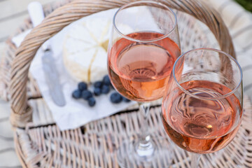 Glasses of delicious rose wine and food on picnic basket outdoors, closeup