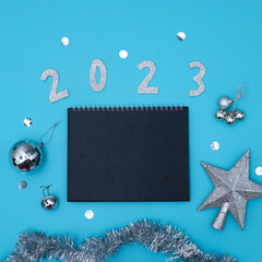 2023 text with blank note for to do list and festive sparkling ornaments on blue background.