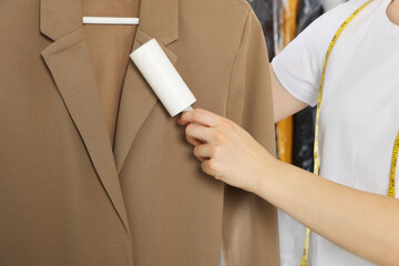 Woman using adhesive lint roller indoors, closeup. Dry-cleaning service