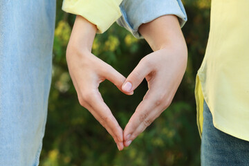Couple making heart with hands outdoors on sunny day, closeup