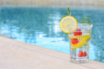 Delicious refreshing lemonade with raspberries near swimming pool, space for text