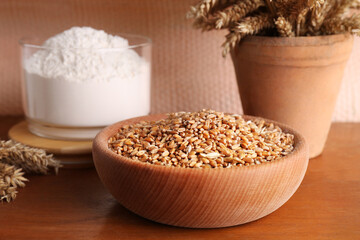 Wheat grains in bowl, spikes and flour on wooden table