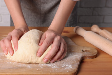Woman kneading dough at wooden table near white brick wall, closeup