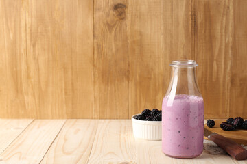 Obraz na płótnie Canvas Delicious blackberry smoothie in glass bottle and fresh berries on wooden table. Space for text