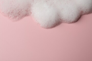 Fluffy soap foam on pink background, above view. Space for text
