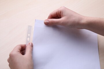 Woman putting paper sheet in punched pocket at wooden table, closeup