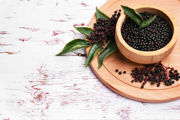 Tasty elderberries (Sambucus) on white wooden table, space for text