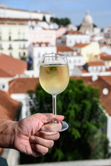 Hand with glass of cold white Portuguese wine in outdoor cafe at view point on old part of Lisbon city, Portugal