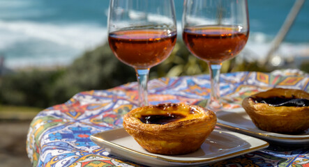 Portugal's traditional food and drink, glasses of porto wine or muscatel and sweet dessert Pastel de nata egg custard tart pastry served with view on blue Atlantic ocean in Lisbon area, Portugal