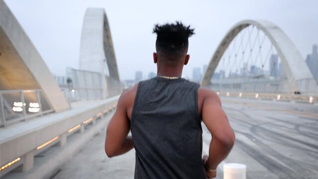 African American man working out by jogging across the 6th Street Bridge in Los Angeles at dawn on an overcast morning. Downtown LA can be seen in the background. Jogger has a deformed left hand.