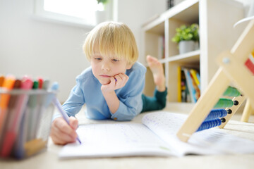 Elementary student boy doing homework on floor at home. Child learning to count, solves arithmetic...