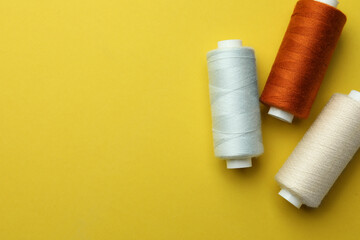 Different colorful sewing threads on yellow background, flat lay. Space for text