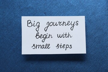 Card with phrase Big Journeys Begin With Small Steps on blue background, top view. Motivational...