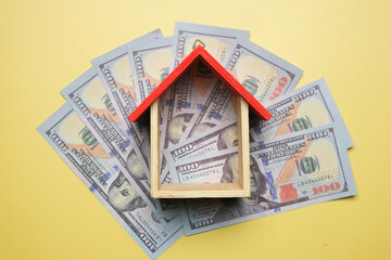 Flatlay picture of house miniature with fake money on yellow background.  Property gain, risk and...