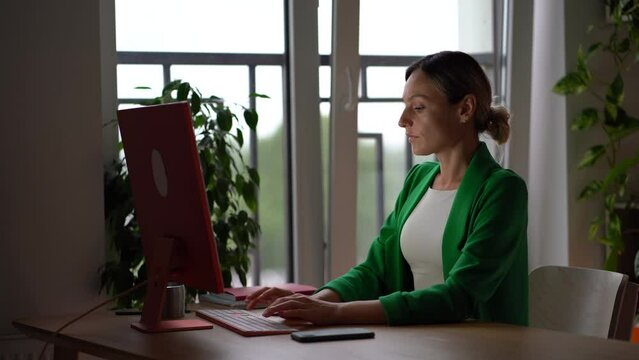 Professional European woman secretary quickly typing email on keyboard performs task of director of company. Business girl in stylish clothes check notification in mobile phone sit at office table