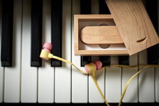 flash drive wooden box yellow headphones put on piano keyboard The headphone cable is arranged into a sound wave.
