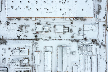 aerial top view of industrial district in winter with snow-covered manufacturing buildings and warehouses.