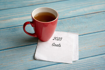 New year 2023 goals on napkin, next to cup of coffee. High angle view.