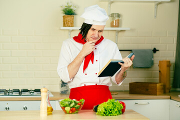 Young man dressed as chef reading recipe book in kitchen. Concept of food, cooking, recipes.