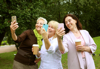 Obraz premium Women taking selfie in summer park. Three senior ladies laughing. Friendship is priceless.